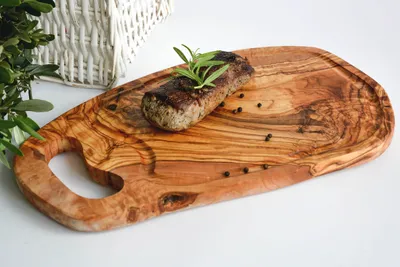 A wooden cutting board with a steak and rosemary on it, with a basket in the background.