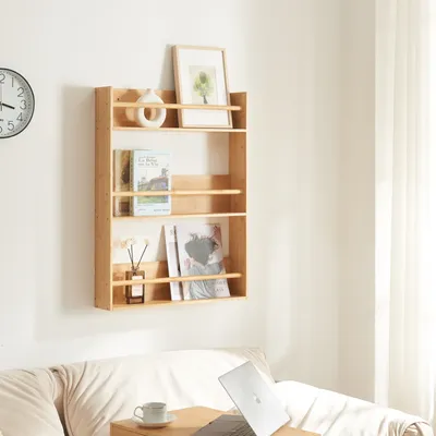 A wooden wall shelf with books, a vase, and a framed picture, placed above a sofa with a laptop and a cup on a small table.