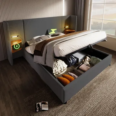 A modern bedroom with a large bed featuring storage underneath, bedside tables with charging ports and lamps, and a window in the background.