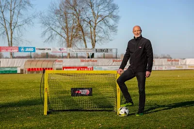 A man stands on a soccer field next to a small soccer goal and a soccer ball.