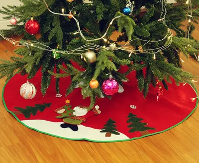 A Christmas tree skirt with festive decorations is shown on a wooden floor.