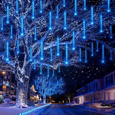 A snowy street at night decorated with blue icicle lights on trees and houses.