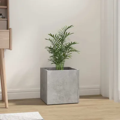 A square concrete-gray planter with a green plant inside, placed on a wooden floor next to a desk.
