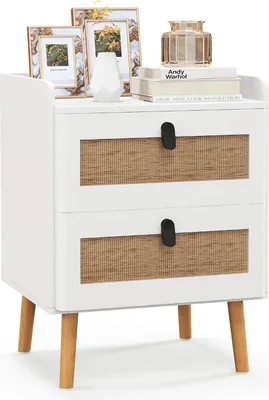 A white nightstand with two drawers featuring woven fronts and wooden legs, decorated with picture frames, a vase, and books on top.