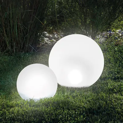Two illuminated spherical garden lights are placed on a grassy lawn with tall reeds in the background.