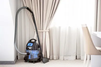 A vacuum cleaner is placed in a corner next to a window with curtains.