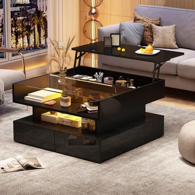 A modern living room with a black hydraulic coffee table with a lift-top, LED lighting, and storage drawers, placed on a gray carpet. The table is decorated with books, vases, and other decorative items. A sofa and a window with a city view are visible in