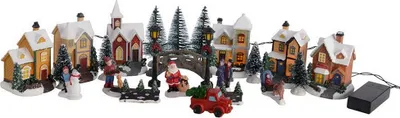 A festive Christmas village scene with illuminated houses, trees, and figures.