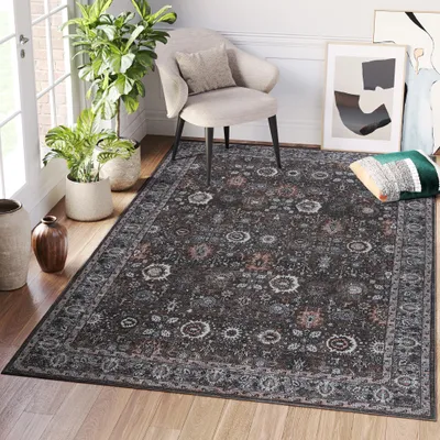 A rug is placed on a wooden floor in a room with a chair, plants, and artwork.