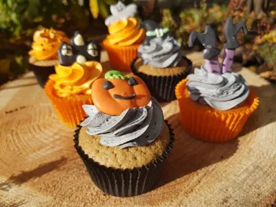 Halloween-themed cupcakes arranged on a wooden surface with foliage in the background.