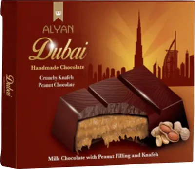 A box of Alyan Dubai handmade chocolates, showing a cross-section of a chocolate bar with peanut filling and knafeh, and a silhouette of Dubai landmarks in the background.