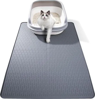 A cat is sitting in a litter box on top of a gray litter mat.