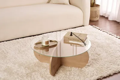 A coffee table with a book and candle on it, placed on a fluffy rug next to a sofa.