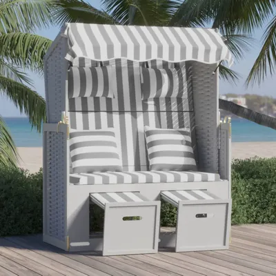 A beach chair with striped cushions is set up on a wooden deck near a beach with palm trees.