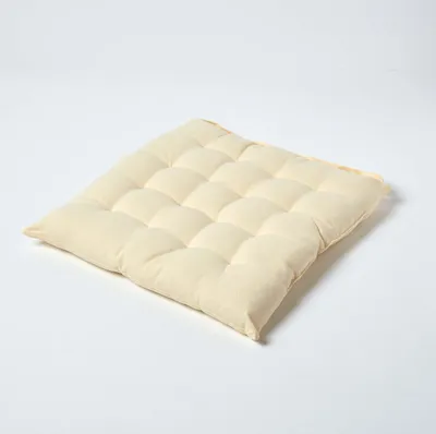 A cream-colored square seat cushion with a tufted surface is placed on a white background.