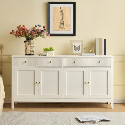 A white sideboard with drawers and doors, decorated with a vase of flowers, a bowl of grapes, and framed pictures.