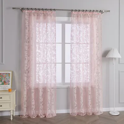 A room interior with pink sheer curtains hanging over a window, a white dresser with a framed picture, and a white floor lamp.