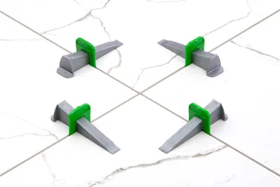 Four tile leveling wedges are placed on a tiled surface, with their green clips inserted between the tiles.