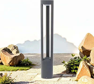 A modern gray outdoor lamp stands in a garden setting with rocks and gravel.