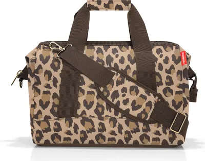 A leopard print duffel bag with brown straps and a detachable shoulder strap.