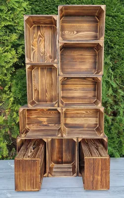 A stack of wooden crates arranged in a display against a green hedge background.