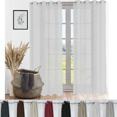A room interior with white sheer curtains hanging over a window, a decorative basket with towels, and a framed picture on the wall.