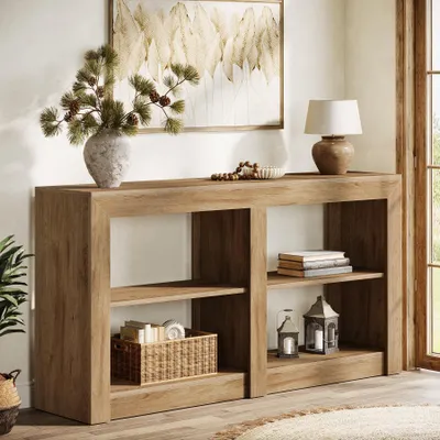 A wooden console table with shelves, decorated with a vase of pine branches, a bowl of beads, a lamp, books, and lanterns.