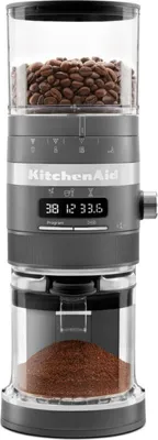 A close-up studio shot of a dark gray KitchenAid coffee grinder filled with coffee beans at the top and ground coffee at the bottom.