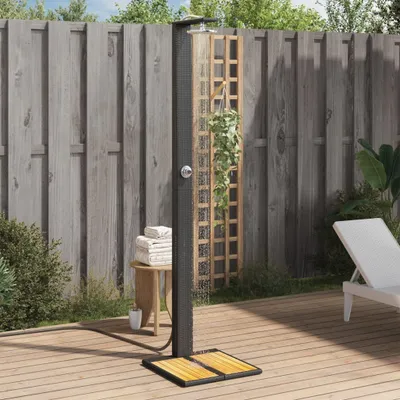 An outdoor shower set up on a wooden deck next to a wooden fence, with plants and a lounge chair in the background.