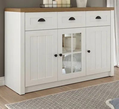 A white sideboard with a wooden top, featuring three drawers and two doors, one of which is a glass-fronted cabinet. It is placed on a wooden floor with a rug in front.