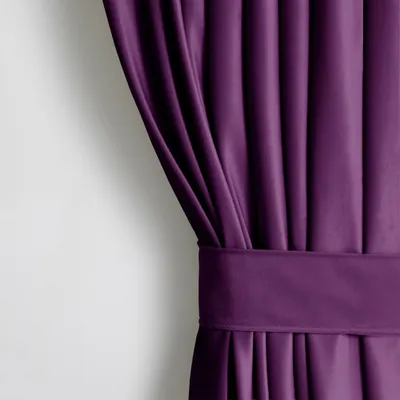 A close-up view of a purple velvet curtain with pleats and a fabric tie.
