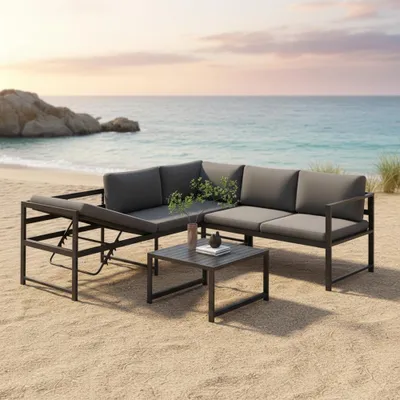 A sectional outdoor sofa with a coffee table set up on a sandy beach next to the ocean.