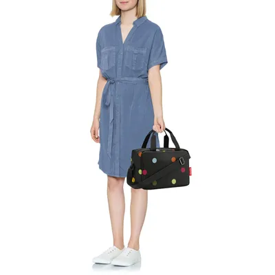 A woman stands against a white background, holding a polka-dot cooler bag.