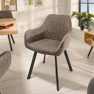 A taupe upholstered chair with diamond stitching and black metal legs is shown in a dining room setting.