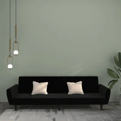 A black two-seater sofa with two striped pillows against a light green wall.