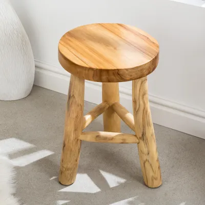 A wooden stool is placed on a light gray floor next to a white vase.