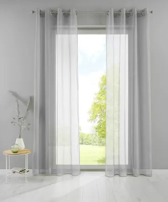 A pair of sheer gray curtains hangs in front of a window, with a small side table and vase to the left.