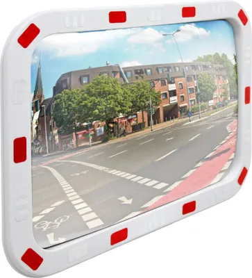 A convex mirror with a white frame and red reflectors, reflecting a street scene with buildings and a road.
