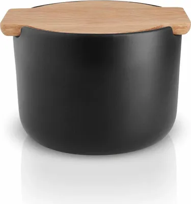 A black ceramic salt cellar with a wooden lid sits on a white reflective surface.