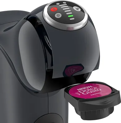 Close-up of a black Dolce Gusto coffee machine with a pink espresso capsule being inserted.
