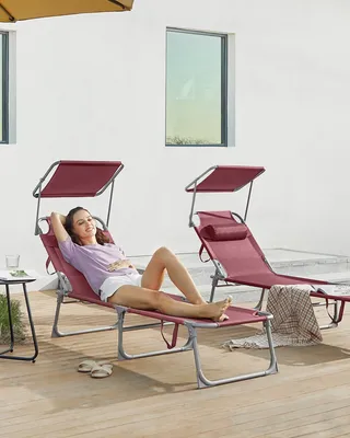 A woman relaxes on a red lounge chair with a canopy, with another lounge chair visible in the background.