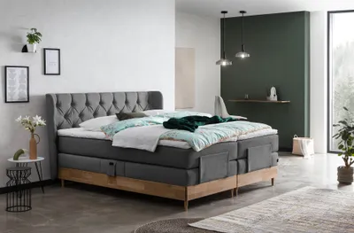A bedroom scene featuring a large boxspring bed with bedding, nightstands, and decorative items.
