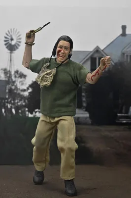 A figure of Leatherface from The Texas Chainsaw Massacre holding a knife and a bloody arm, with a farmhouse and windmill in the background.