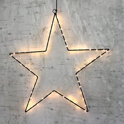 A black wire star outline with warm white LED lights is hanging against a textured gray wall.