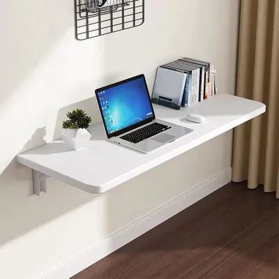 A white folding desk mounted on a wall, with a laptop, a small plant, and books on it.