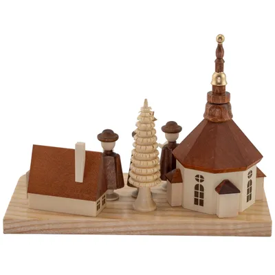 Ein kunstvoll gestalteter Kerzenhalter zeigt ein kleines Dorf mit einer Kirche einem Baum und zwei Figuren auf einer Holzplatte