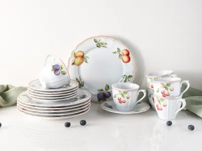 A set of porcelain dishes with fruit illustrations, including plates, cups, and saucers, arranged on a white surface.