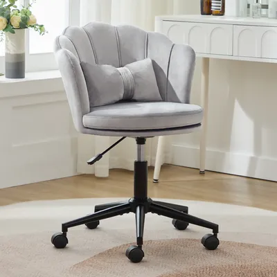 A gray velvet office chair with a scalloped back and a bow-shaped lumbar pillow is shown in a room with a desk and a vase of flowers.