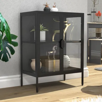 A black glass display cabinet with decorative items inside, placed in a room with a plant and a wall.