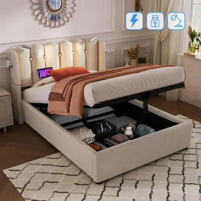 A beige upholstered bed with its storage compartment open, revealing stored items. The bed has a tufted headboard with integrated reading lights and USB ports.